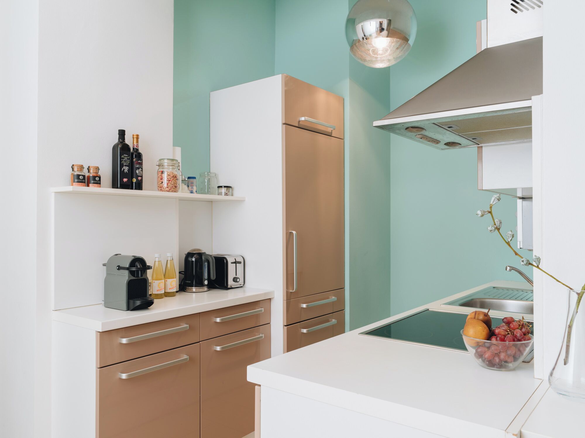 Een moderne keuken met een wit aanrecht, een inbouwoven, een koffiezetapparaat en een schaal met fruit.
