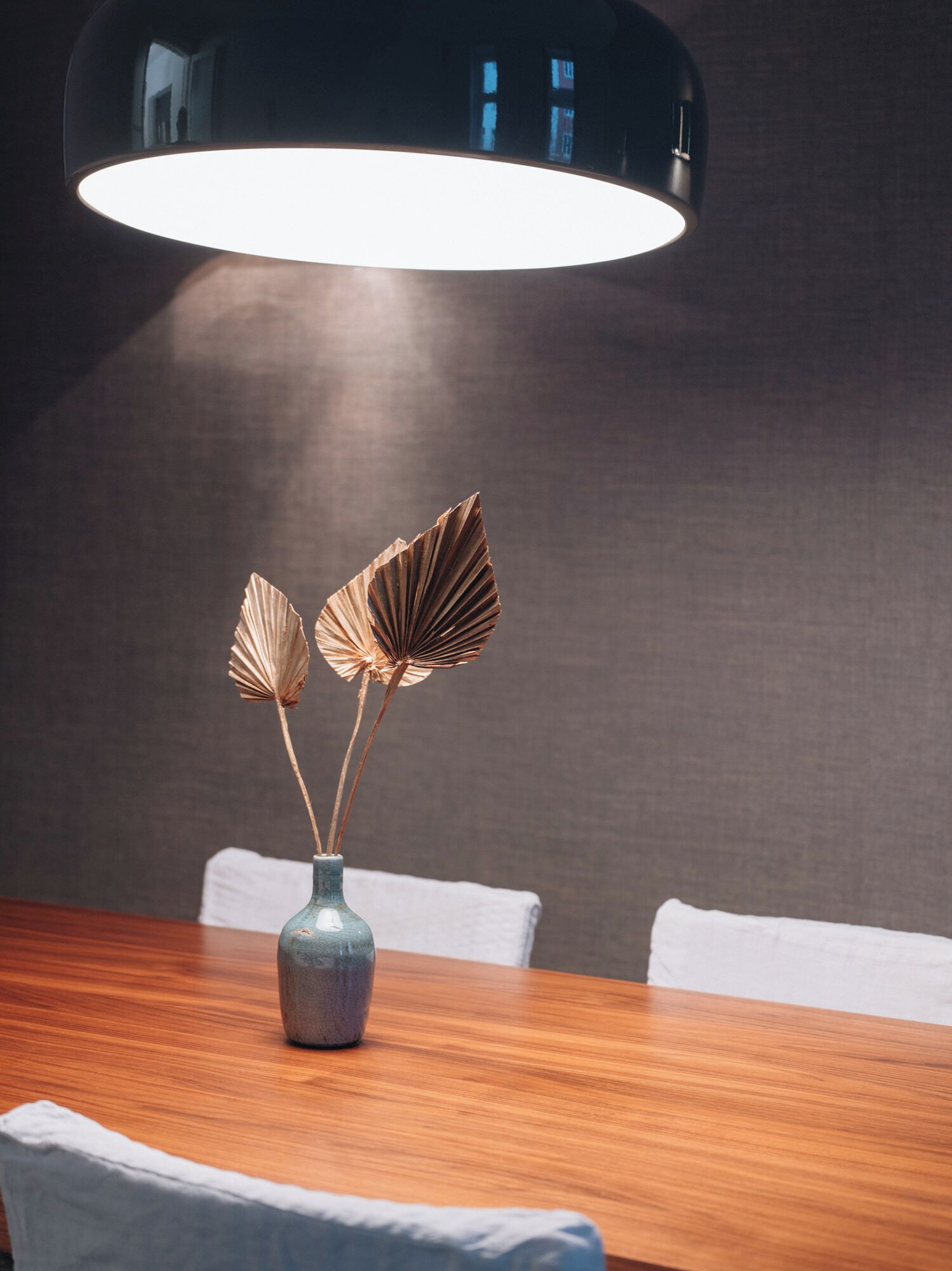 A dining table with a vase of dried flowers and a modern pendant light.