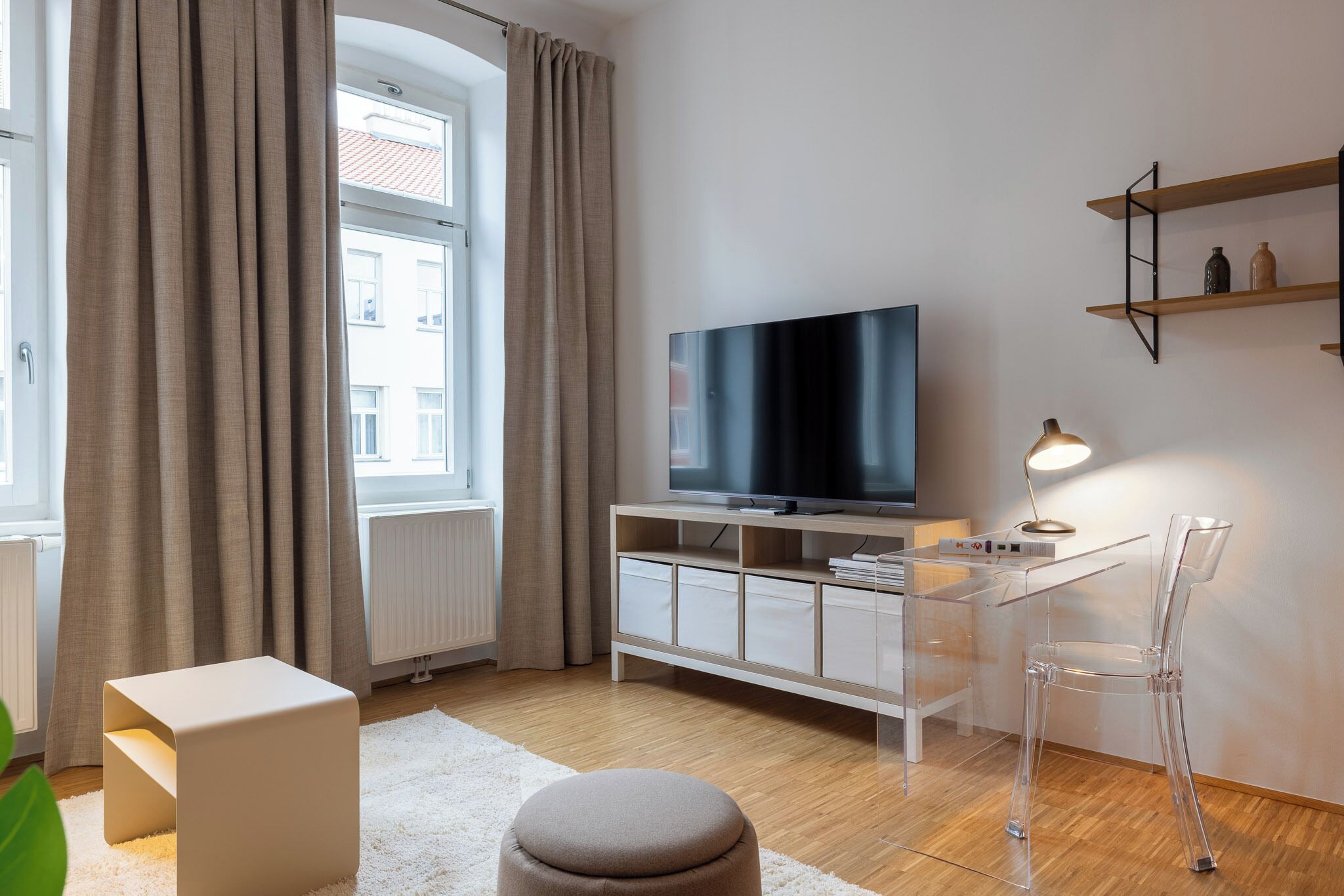 A modern living room with a TV, clear plastic chair, and a white cabinet.