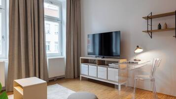 A modern living room with a TV, clear plastic chair, and a white cabinet.