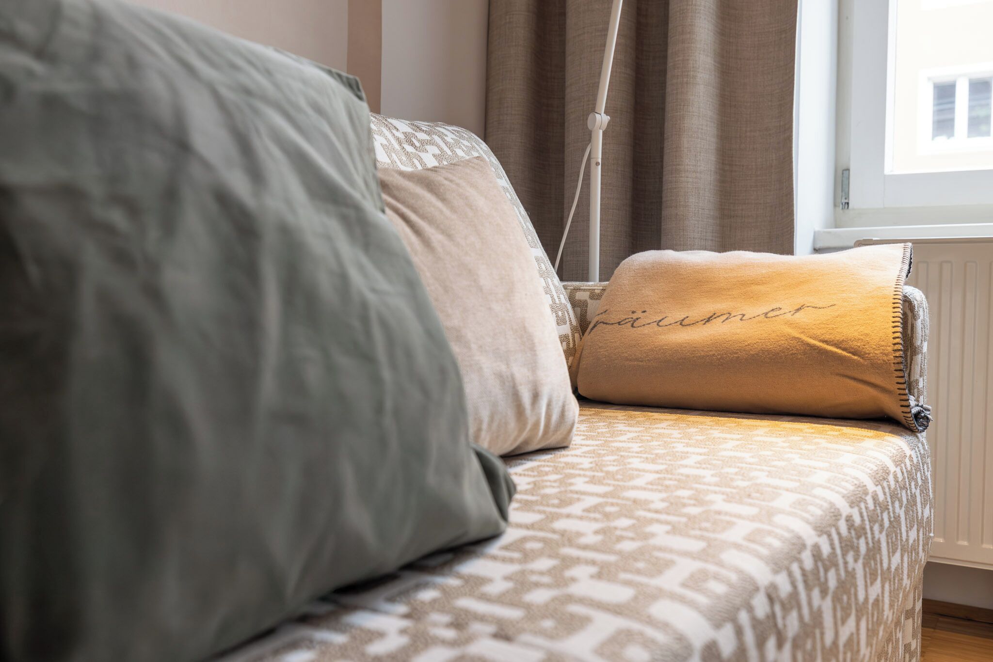 Uma cama com roupa de cama estampada, uma luminária de cabeceira e uma janela com cortinas.