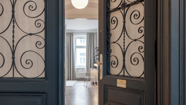 Un pasillo con una puerta oscura, una lámpara y vistas a una habitación con un escritorio y una silla.