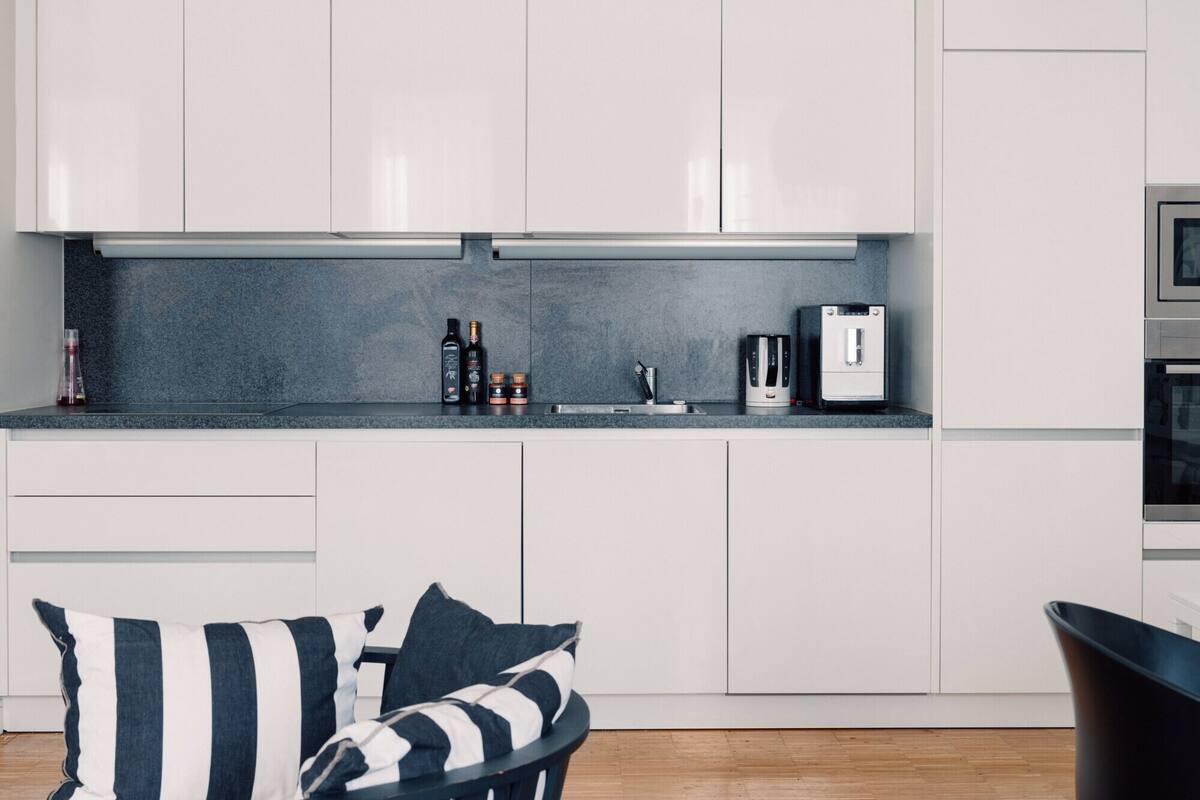 A modern kitchen with white cabinets, a dark countertop, a coffee machine, and a kettle.