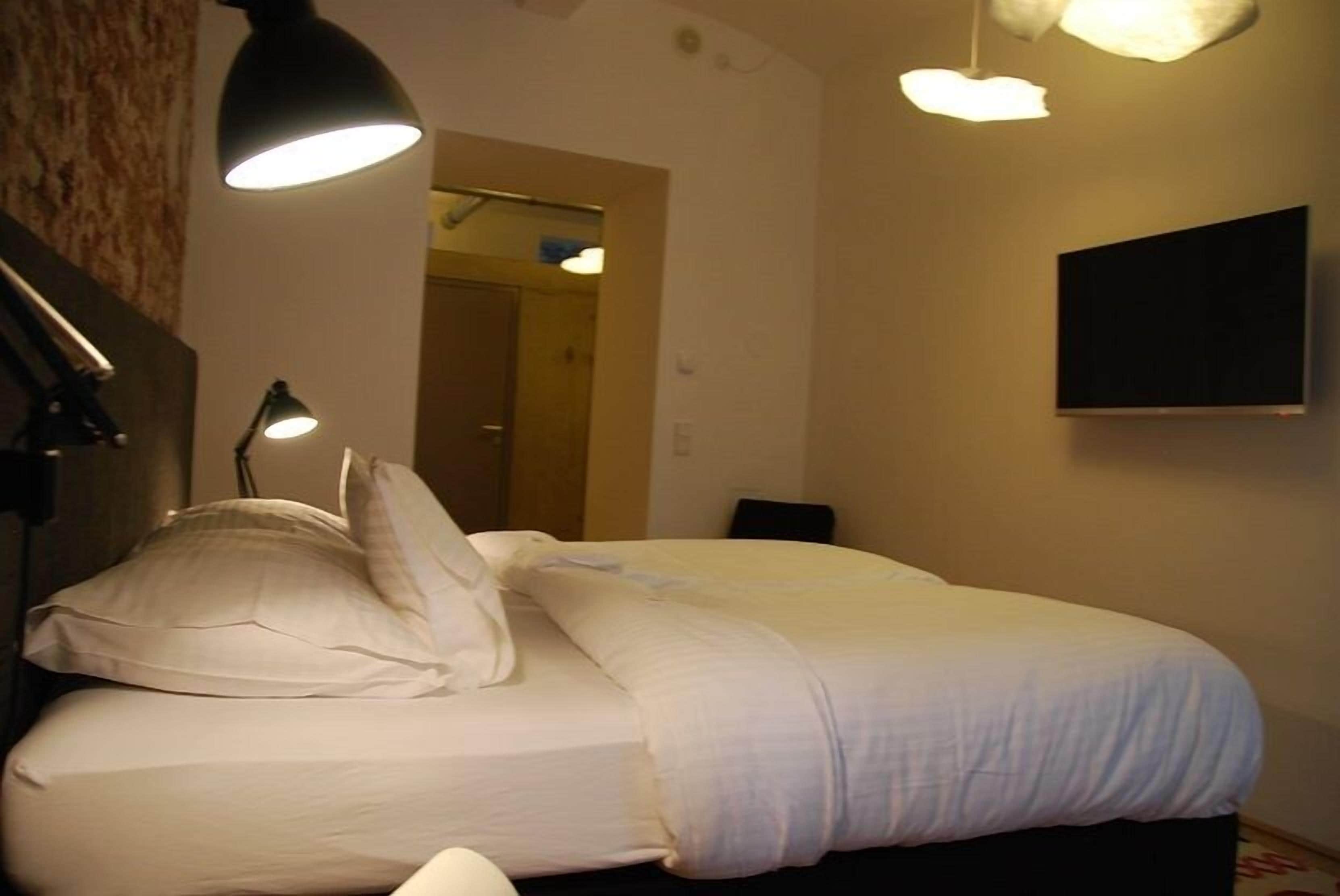 A neatly made bed with white linens, two bedside lamps, and a flat-screen TV mounted on the wall.