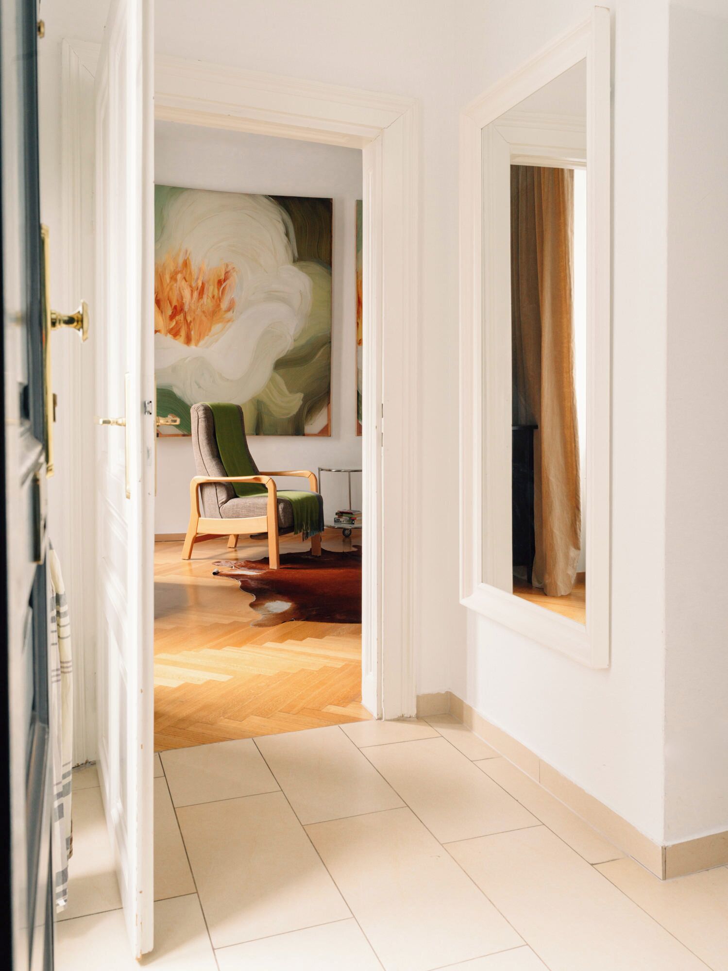 An open doorway leading to a room with a bed, a chair, a painting, and a window with curtains.