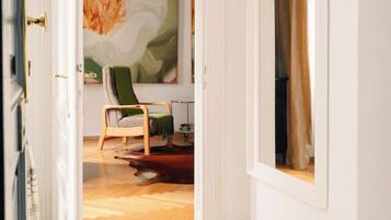 An open doorway leading to a room with a bed, a chair, a painting, and a window with curtains.