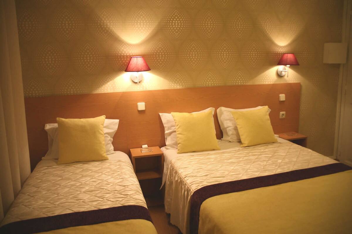 Habitación de hotel con dos camas, cada una con cabecero de madera y una mesita de noche. Hay dos lámparas de pared a cada lado de las camas.