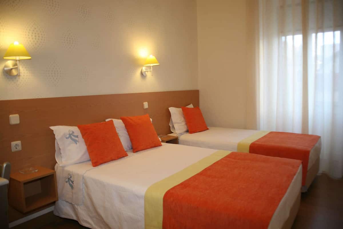 Habitación de hotel con dos camas, cada una con almohadas naranjas y un edredón blanco. Hay dos lámparas de pared a cada lado de las camas.