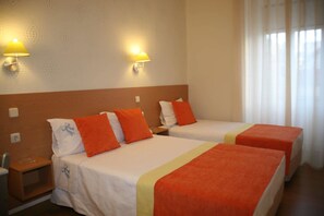 A hotel room with two beds, each with orange pillows and a white bedspread. There are two wall-mounted lamps on either side of the beds. - Estrela dos Anjos (Lisbon)