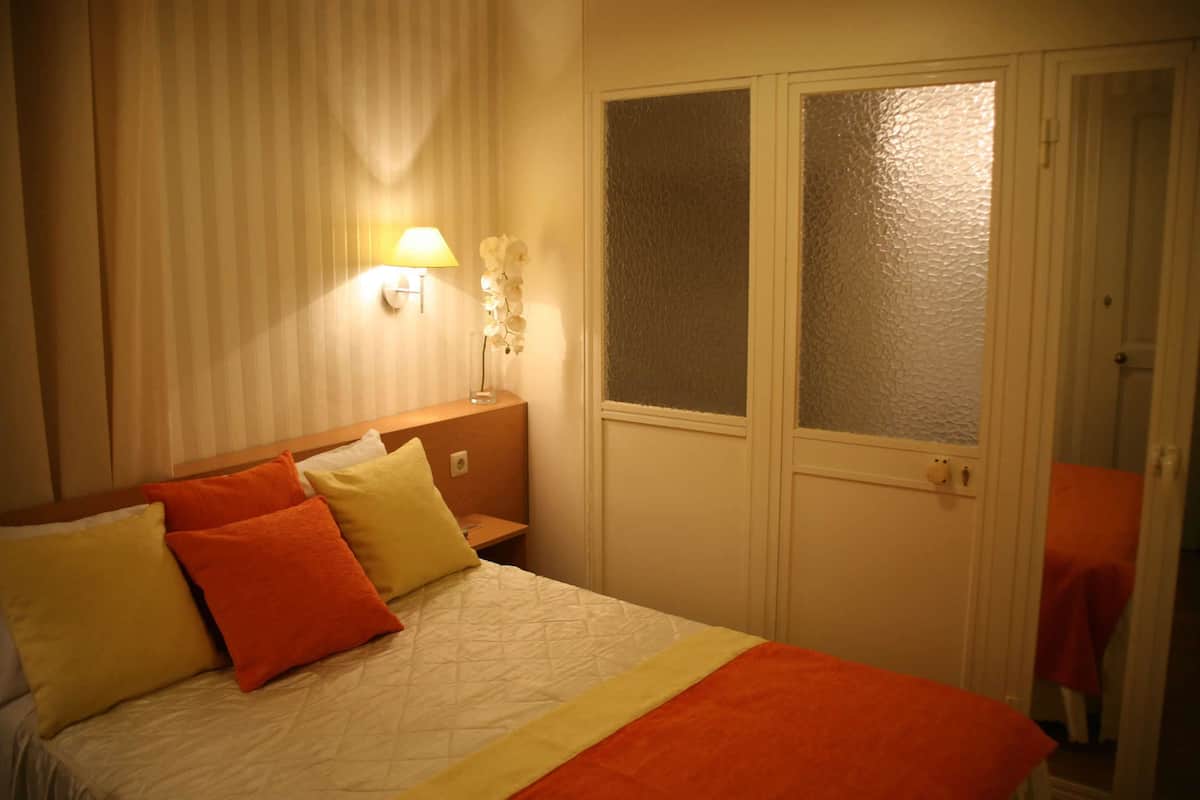 Una habitación de hotel con una cama, mesitas de noche, una lámpara y una puerta de vidrio esmerilado.