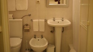 Een compacte, goed verlichte badkamer met toilet, bidet, wastafel en spiegel.