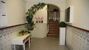 Een hal met betegelde vloer, een witte console tafel met planten en een trap, en een spiegel aan de muur.