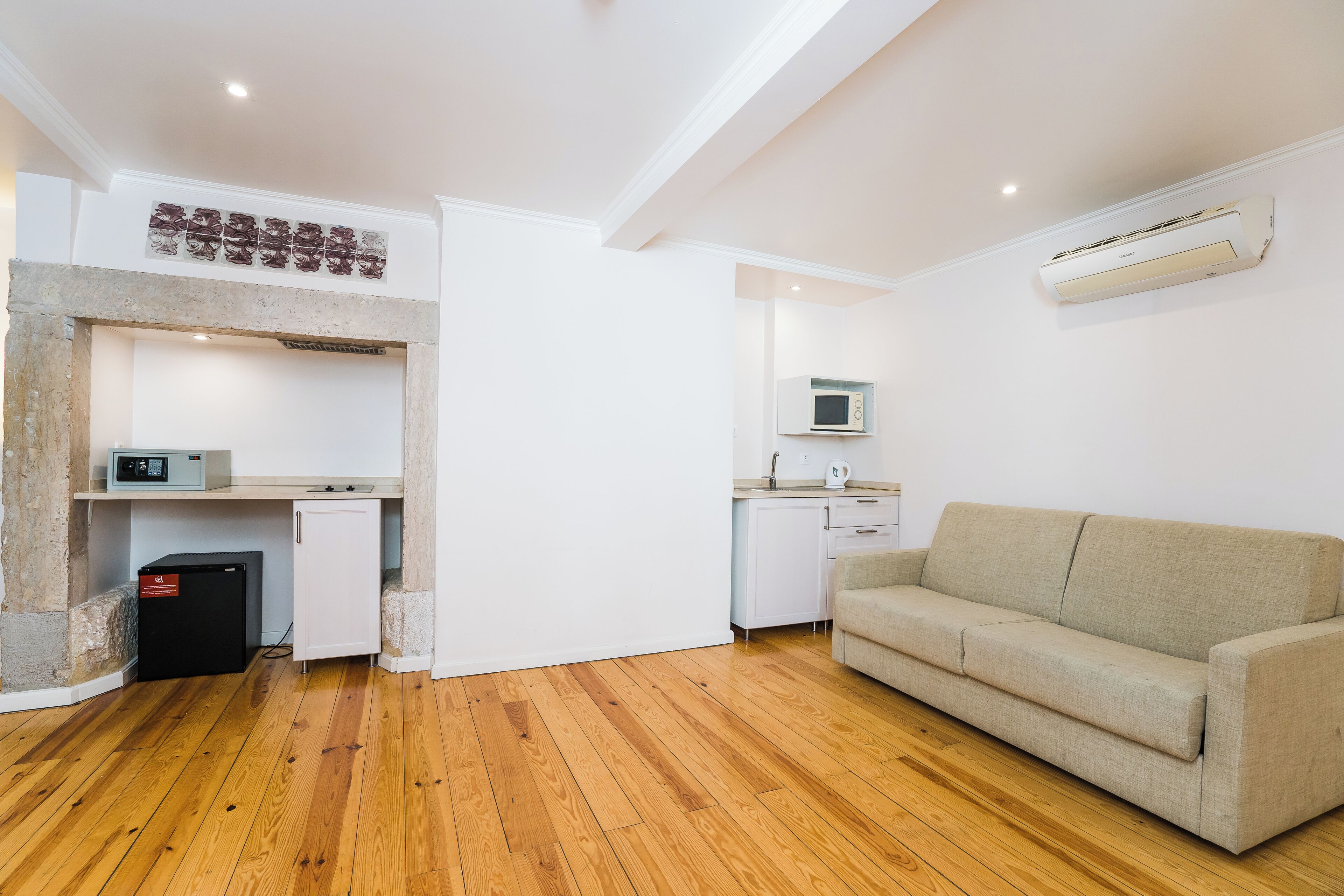 A compact living space with a kitchenette, a sofa, and a built-in air conditioning unit.