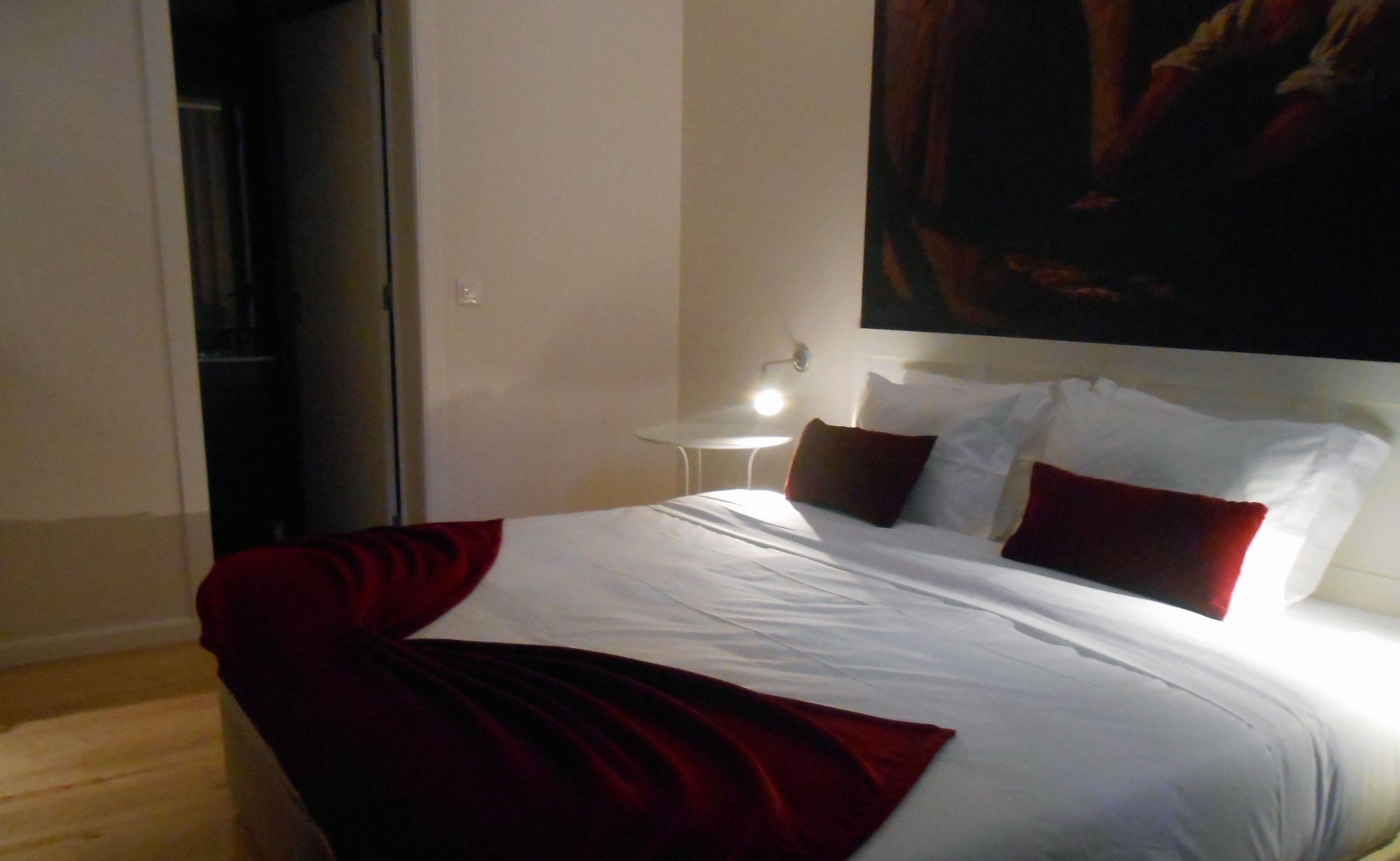 Una habitación de hotel con una cama, una mesita de noche y un cuadro en la pared.