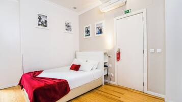 A hotel room with a white bed, red throw blanket, wooden flooring, and three framed pictures on the wall.