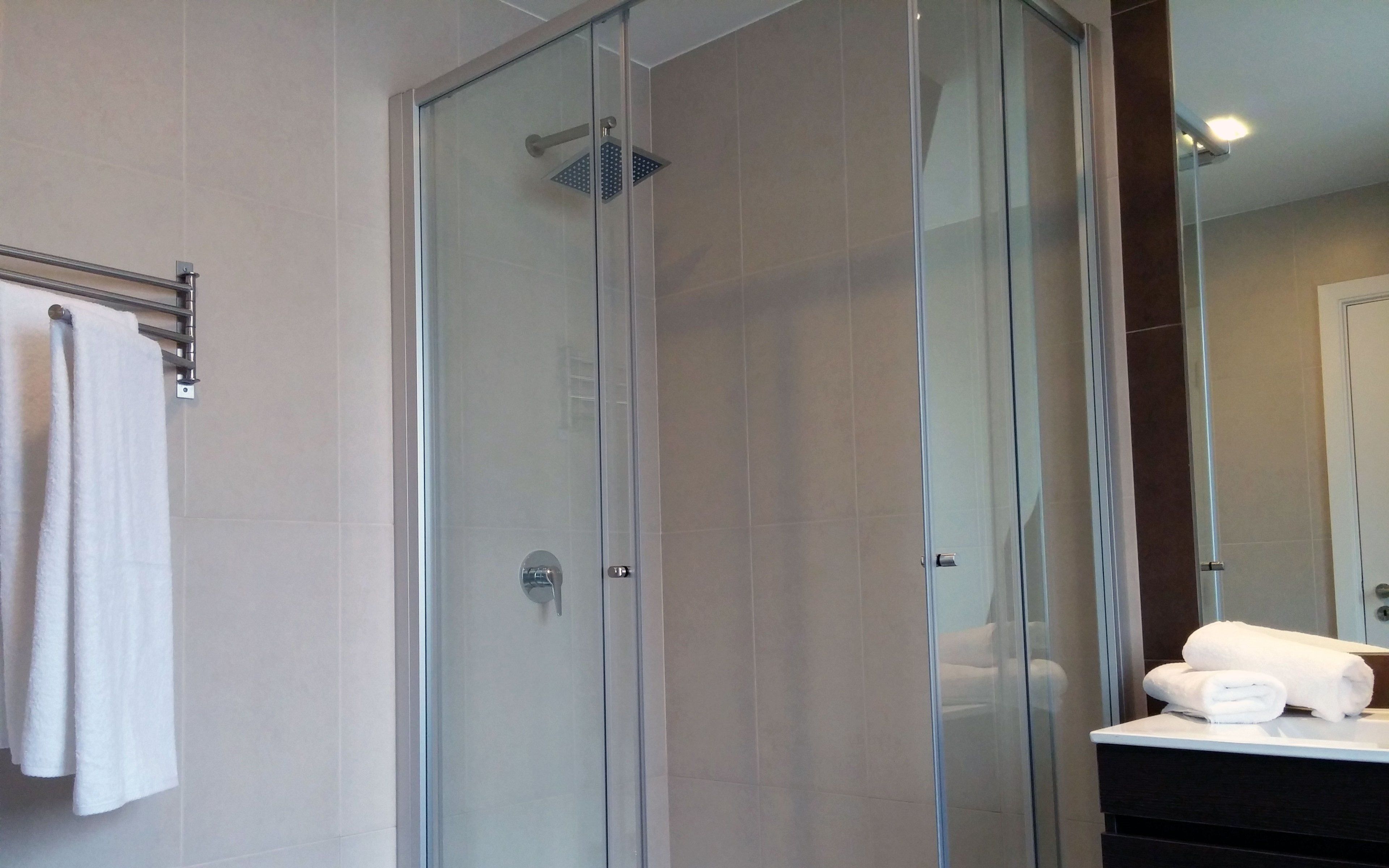 Uma casa de banho moderna com chuveiro envolto em vidro, um porta-toalhas e um espelho refletindo uma toalha branca.