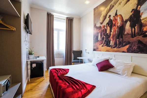 A hotel room with a bed, a desk with a computer, a chair, and a painting on the wall.