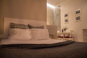 A bedroom with a bed, pillows, a bedside table, a chair, and a small table with a plant.