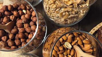 Various bowls of nuts and grains, including almonds, walnuts, and oats, with wooden spoons in them.
