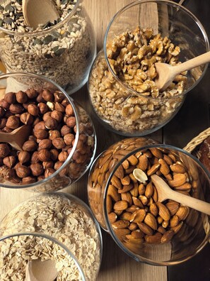Diferentes recipientes con frutos secos y cereales, como almendras, nueces y avena, junto con cucharas de madera.