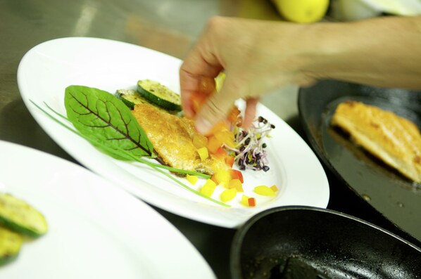 Un cocinero preparando un plato con verduras y pescado sobre un plato blanco.