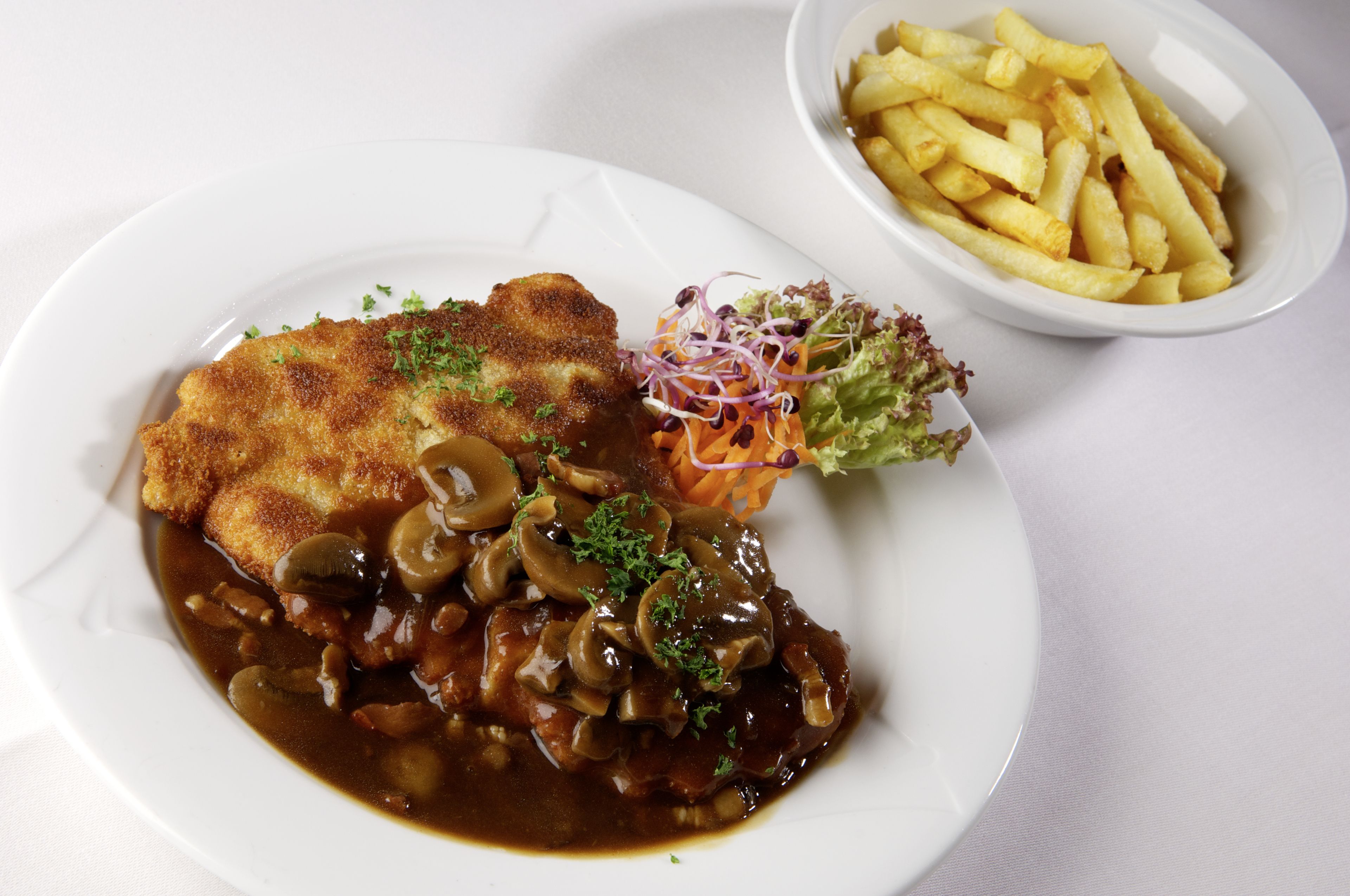 Un plato de comida con milanesa, champiñones y una ensalada.