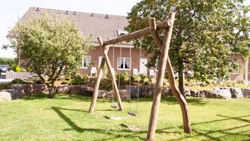 Relax in a serene outdoor space with a permanent swing set, surrounded by a lush lawn and shaded by trees.
