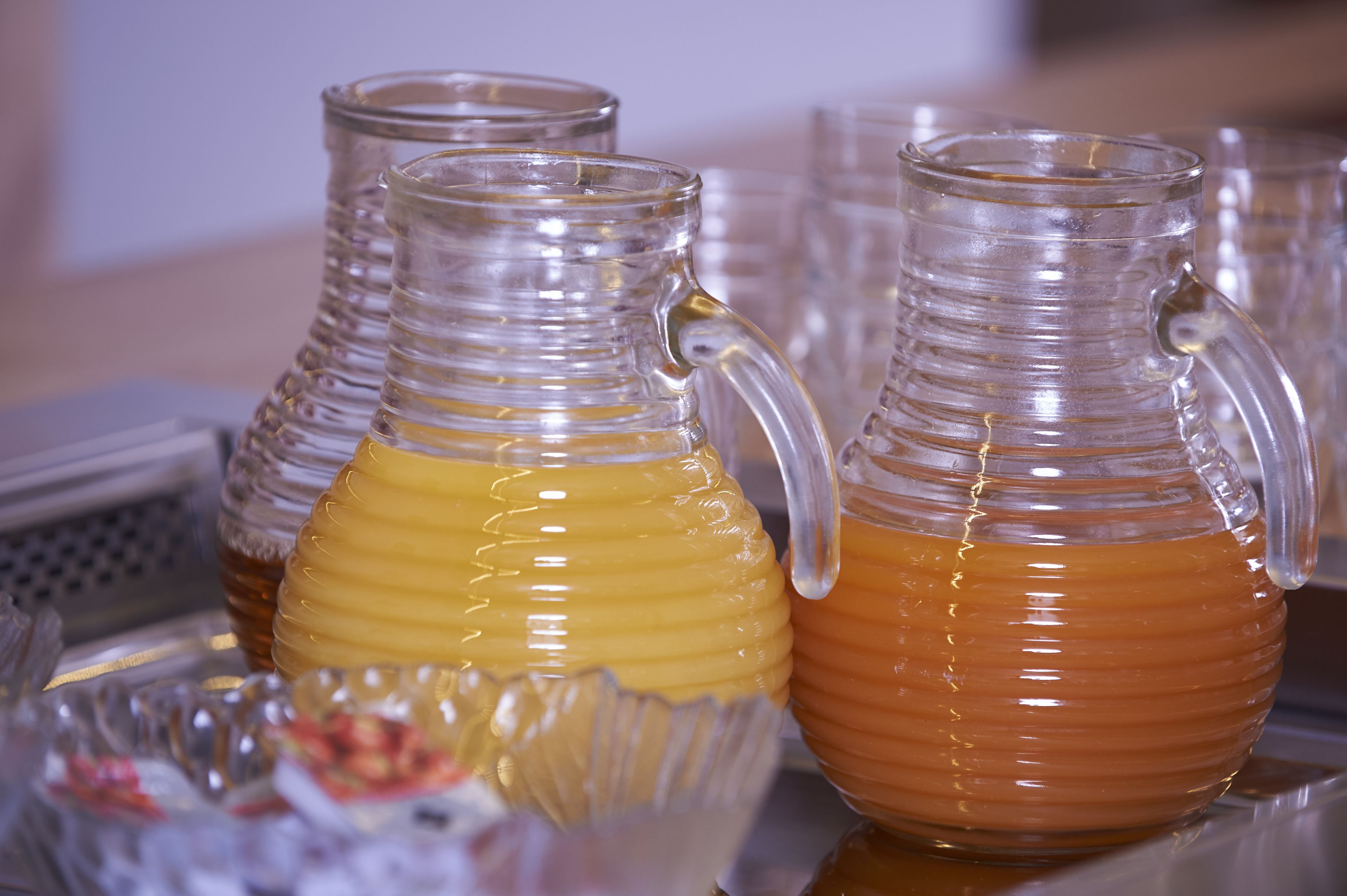 A table with several glass pitchers containing a yellowish liquid, likely honey or syrup, and a small bowl of red fruit.