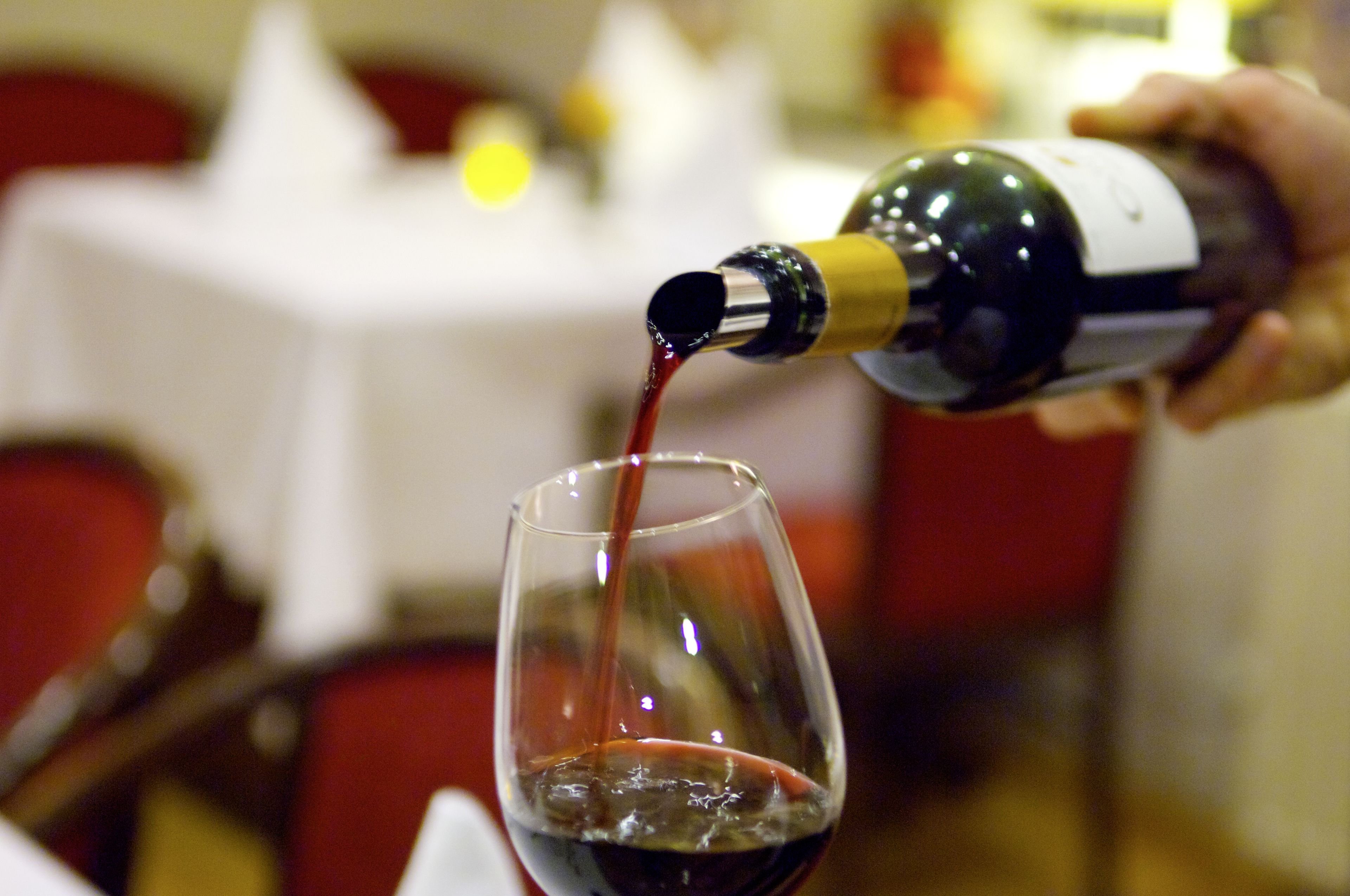 A hand pouring red wine into a glass.