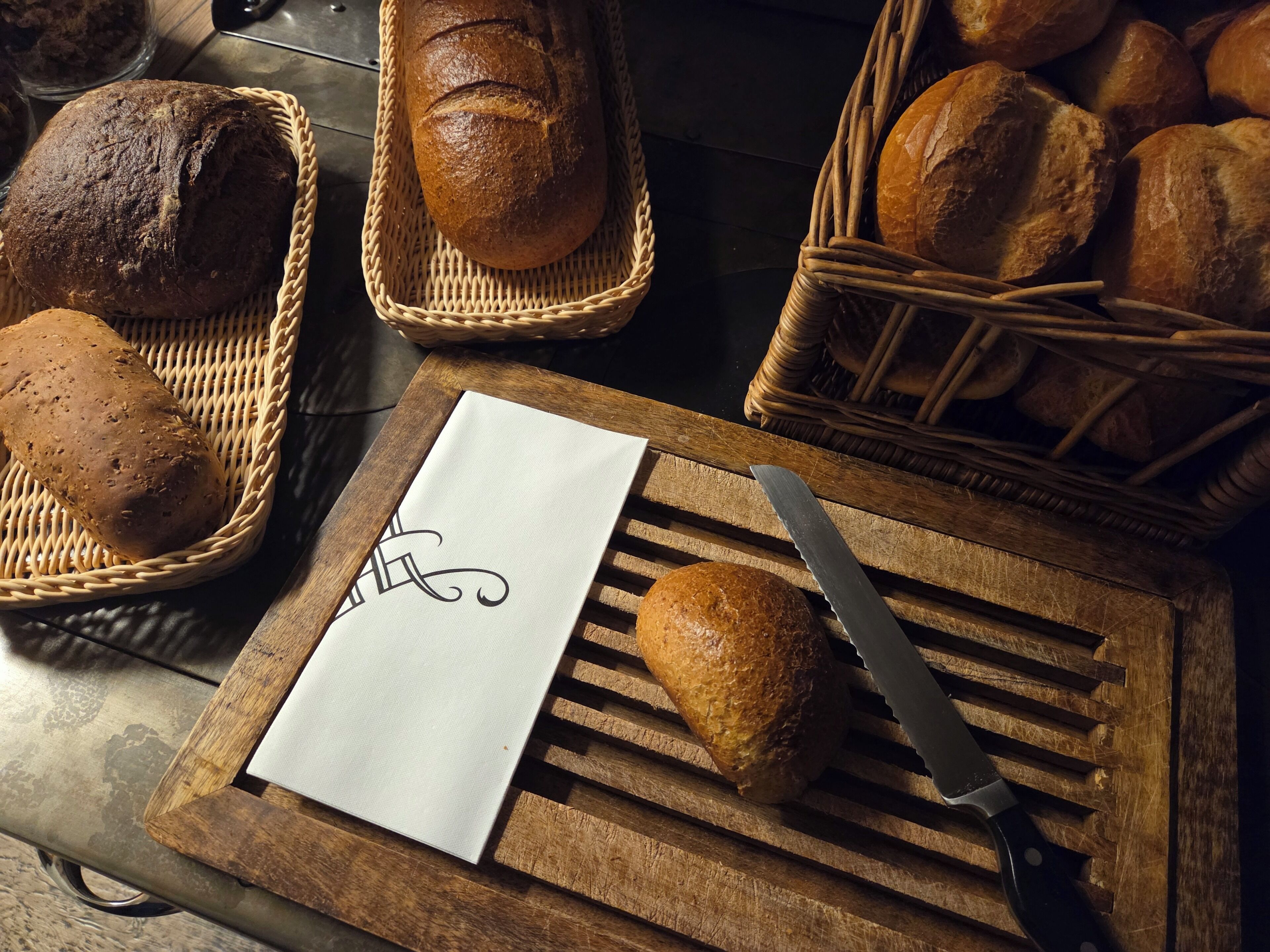 A wooden cutting board with a loaf of bread, a knife, and a napkin with a monogram.
