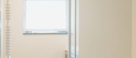 A hallway with a glass shower door, a window, and a metal rack.