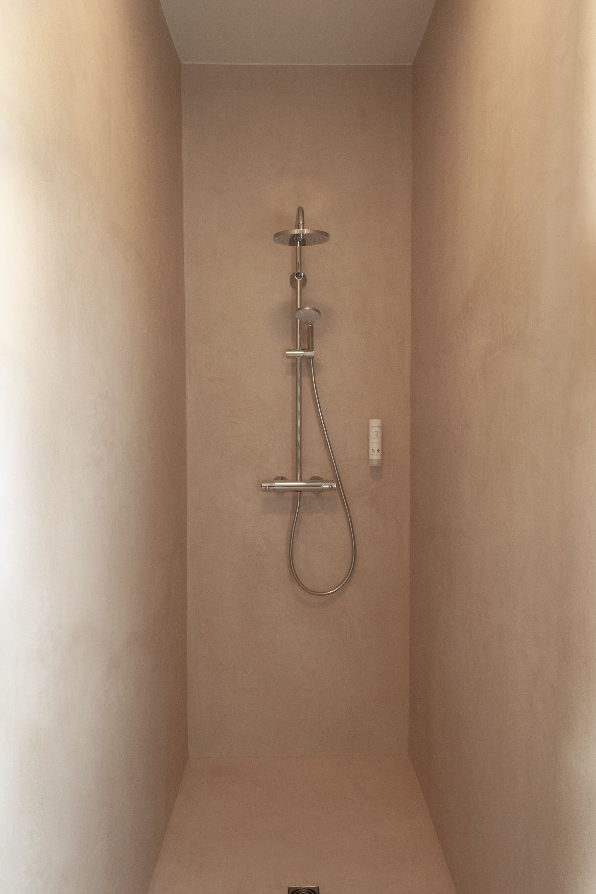 A minimalist shower enclosure with a wall-mounted showerhead and control panel.