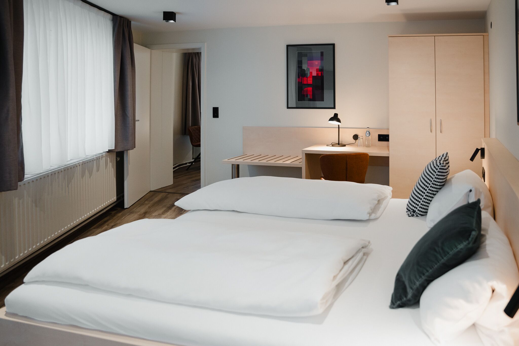 A hotel room with a bed, a desk, and a wardrobe.