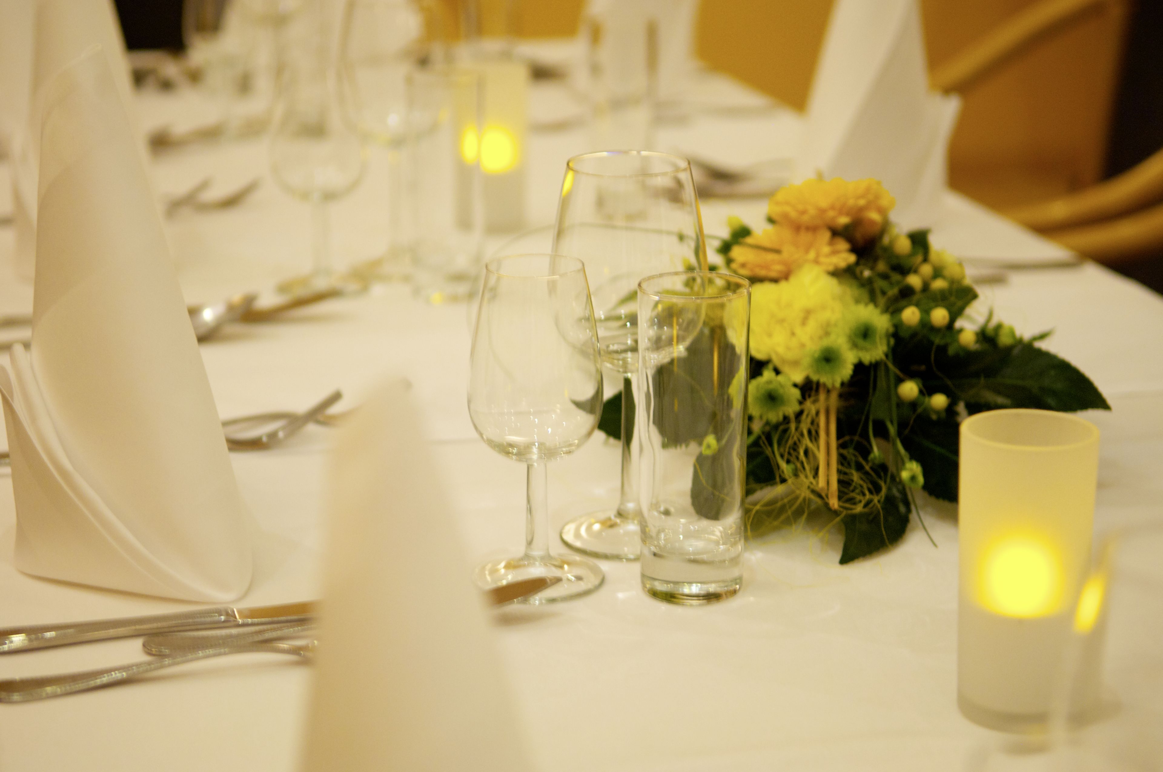 Una mesa dispuesta para comer, con copas transparentes, una vela y un centro de mesa floral.