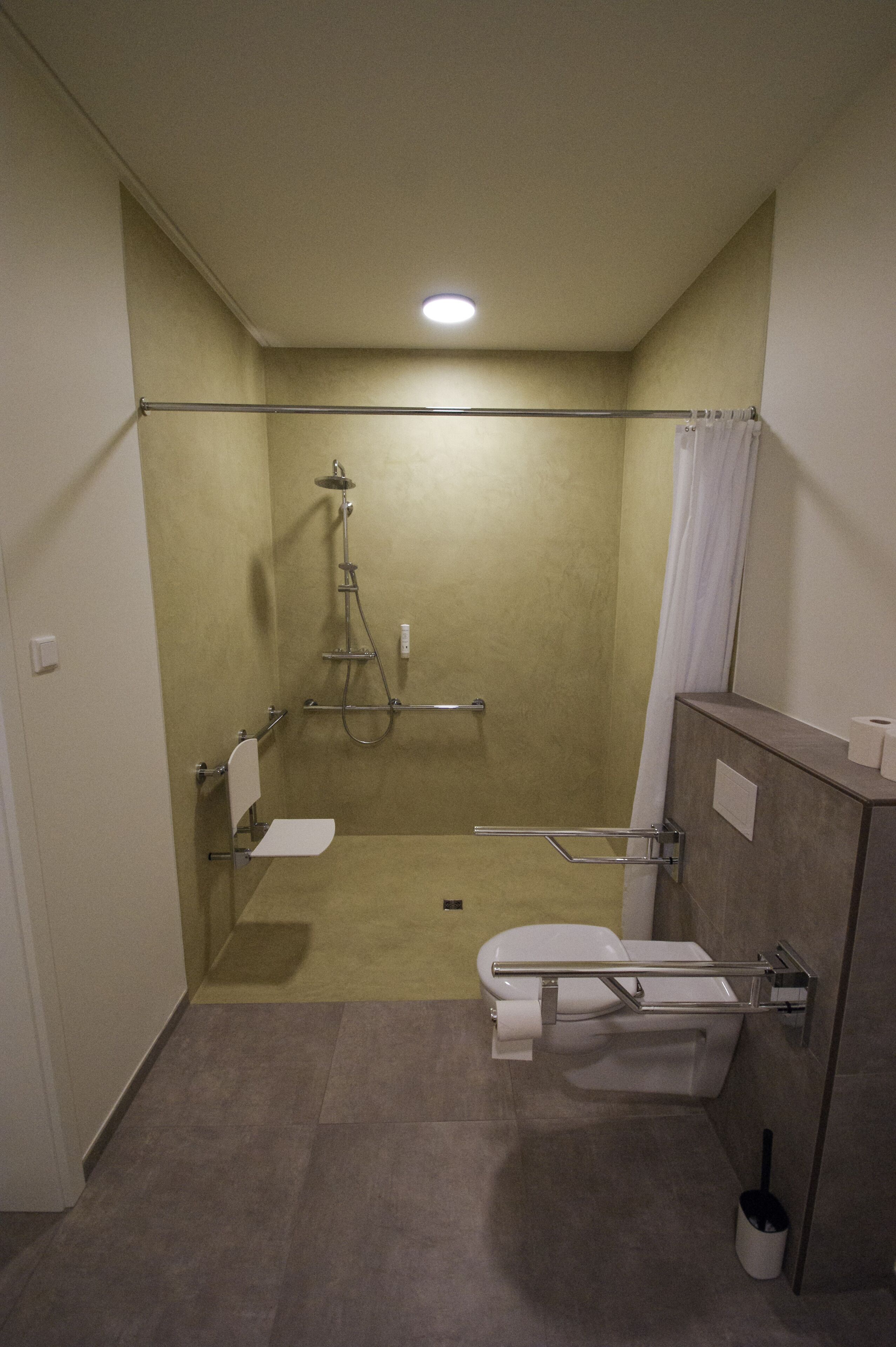 A small, enclosed shower area with a toilet and a grab bar, a towel rack, and a showerhead.