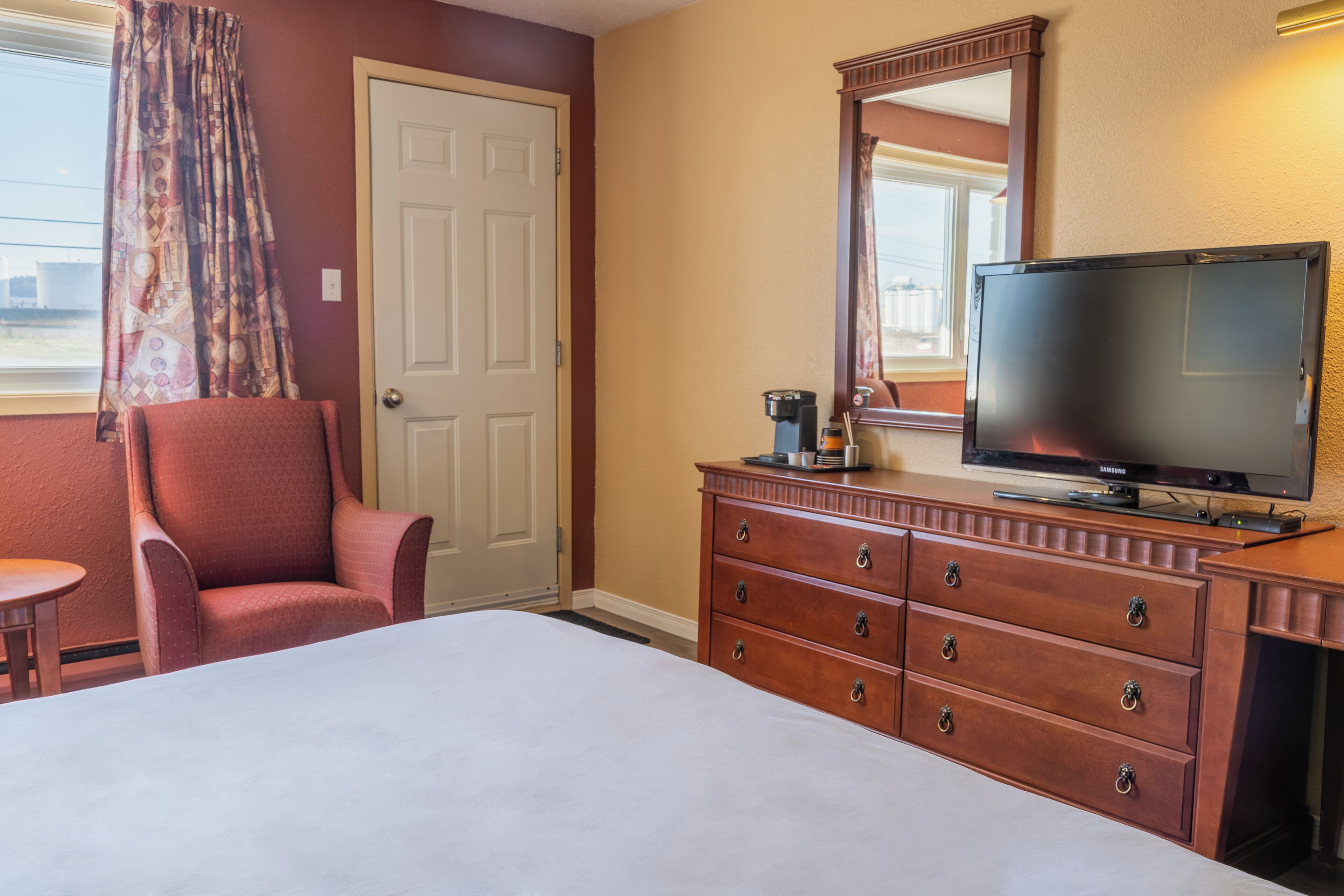 A hotel room with a bed, a wooden dresser, a television, and a chair.