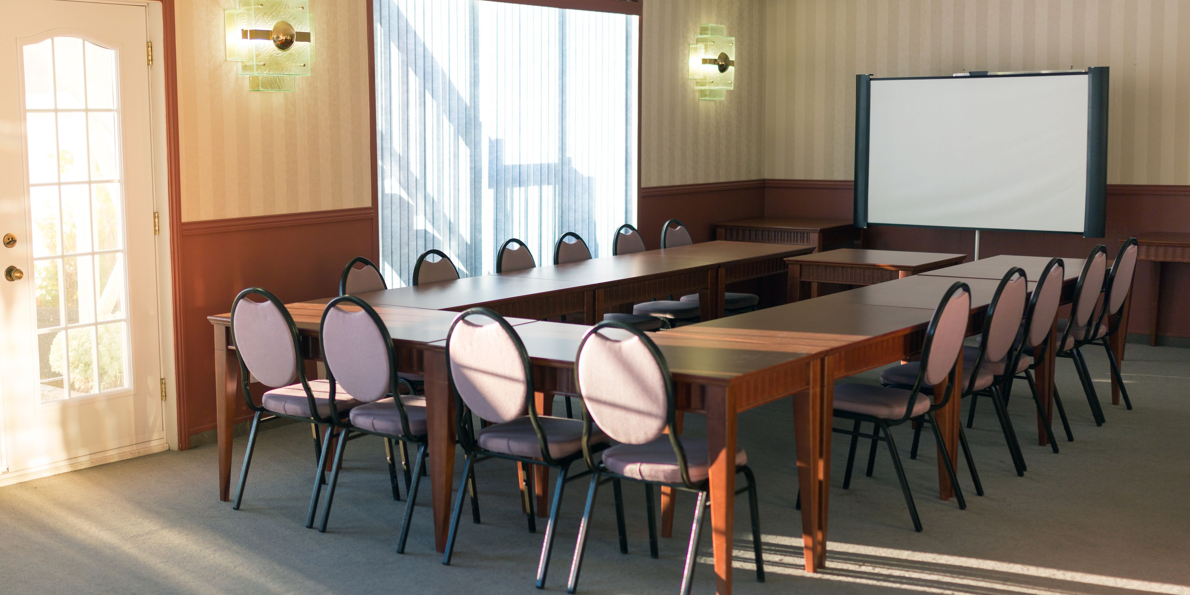 A conference room with a long table, multiple chairs, a whiteboard, and a door with a window.