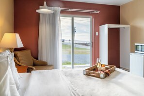 A hotel room with a bed, a chair, a table with a tray of food and drink, a lamp, and a view of the outdoors through a sliding door. - Hôtel Motel La Vigie (Matane)