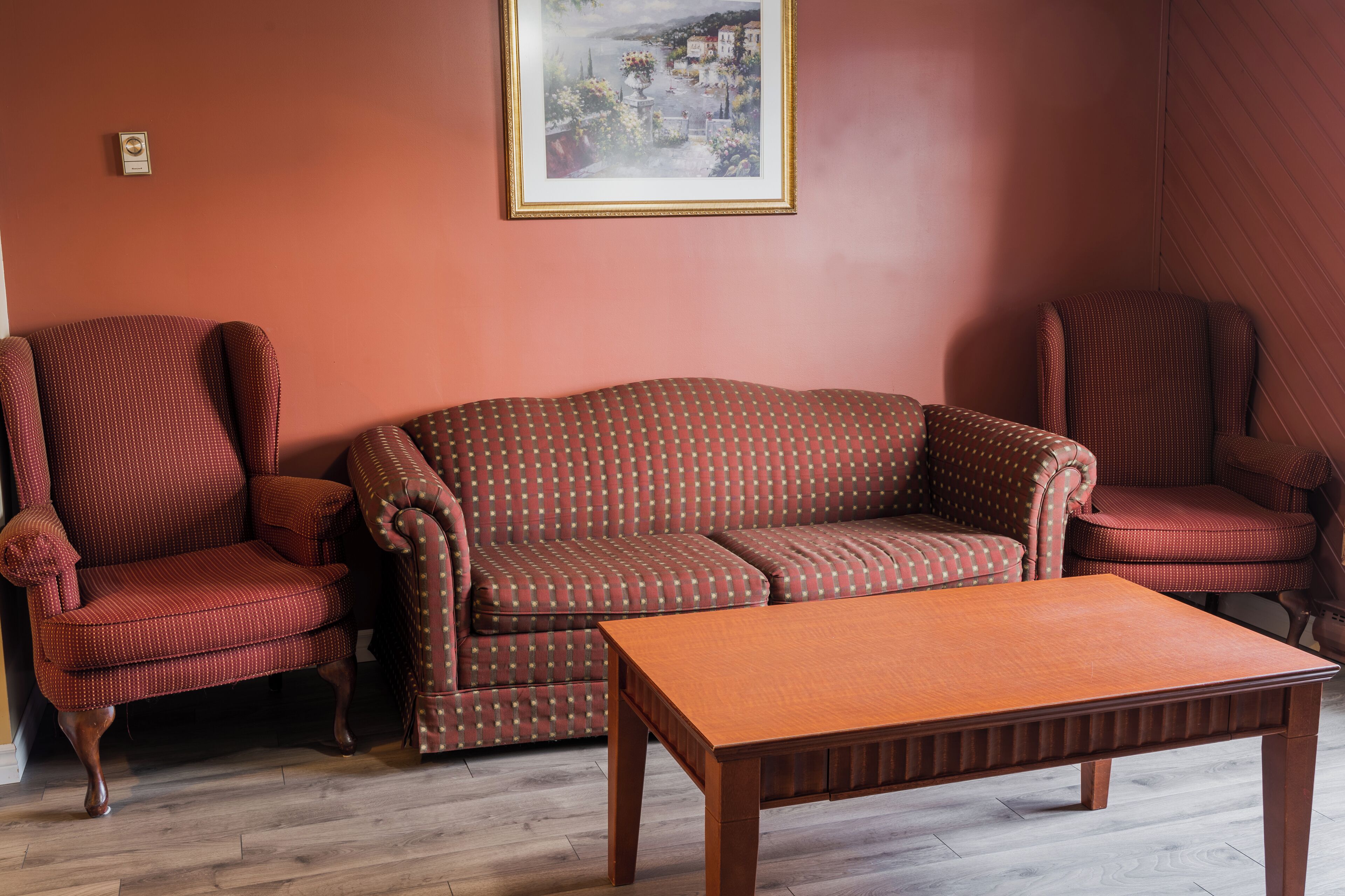 Una habitación con piso de madera, un sofá marrón, dos sillones estampados y una mesa de centro de madera.