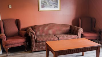 Una habitación con piso de madera, un sofá marrón, dos sillones estampados y una mesa de centro de madera.