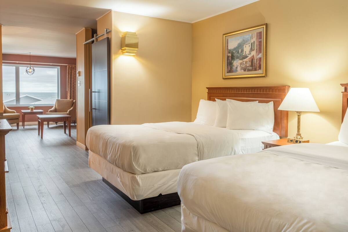 Quarto de hotel com duas camas, cabeceira de madeira, um quadro na parede e vista para o mar pela janela.