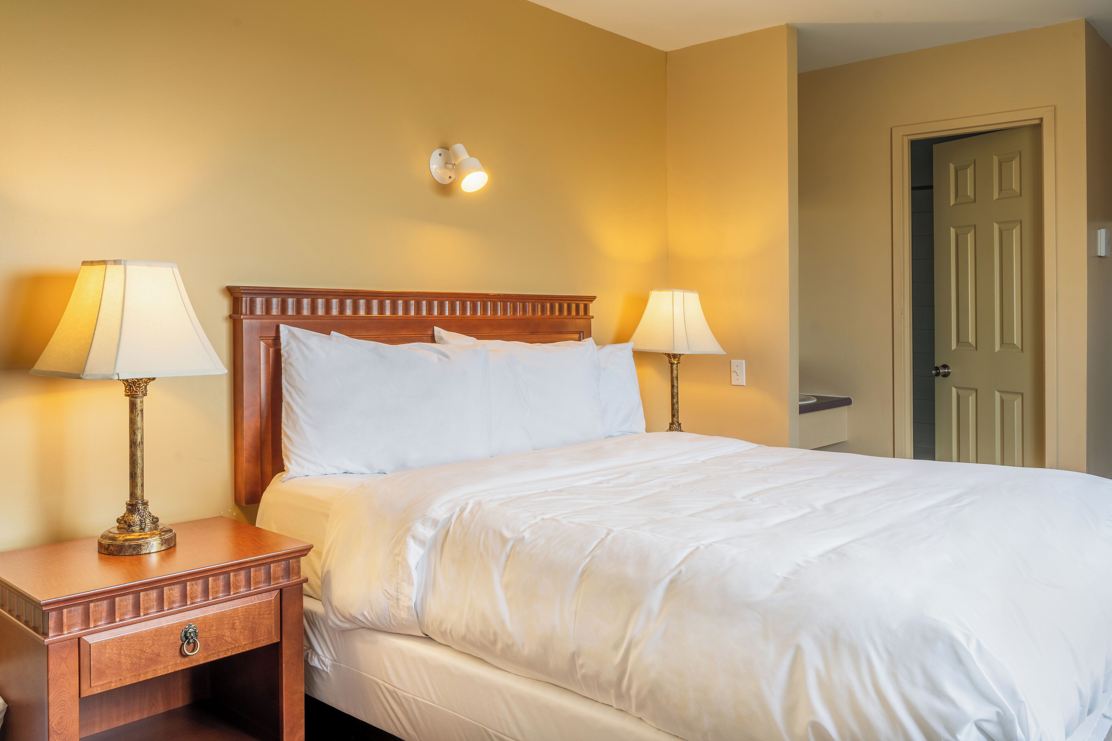 Een hotelkamer met een bed, twee bedlampen, een nachtkastje en een deur.
