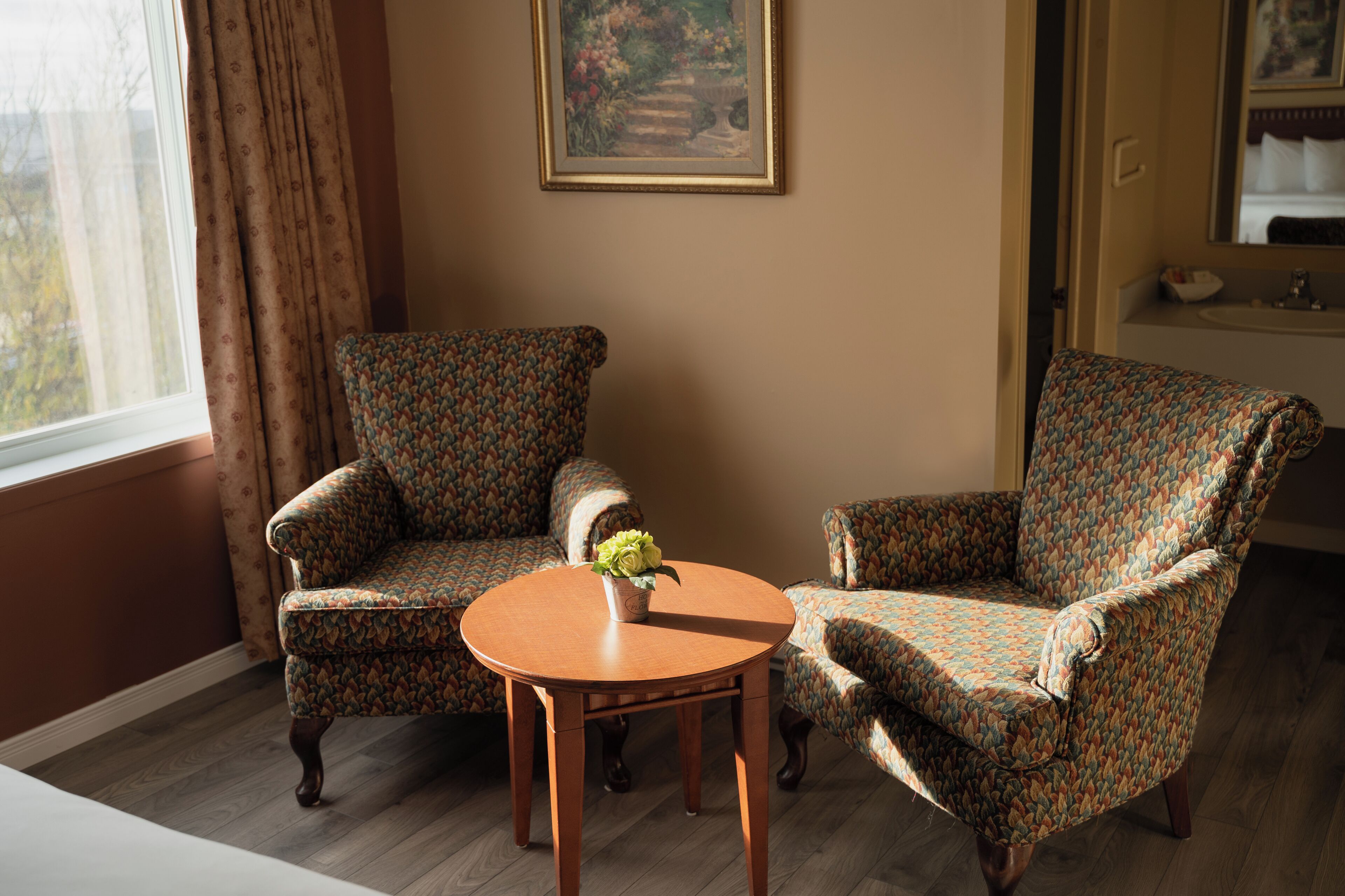 Une pièce comprenant deux fauteuils à motifs, une petite table en bois et un tableau accroché au mur.