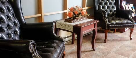 Una habitación con dos sillones de cuero negro, una mesa de madera con un centro de mesa floral y una estantería al fondo.