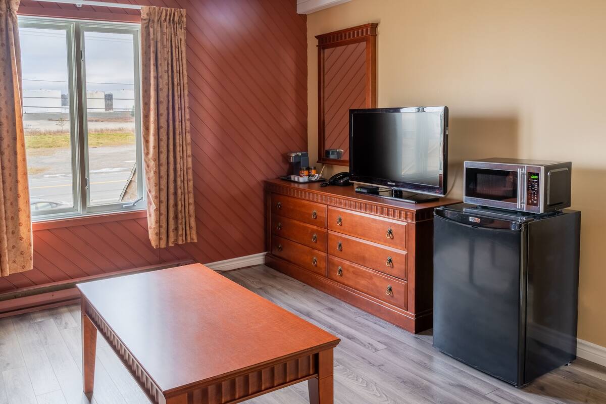 Quarto compacto com cômoda de madeira, televisão, micro-ondas e pequena geladeira.