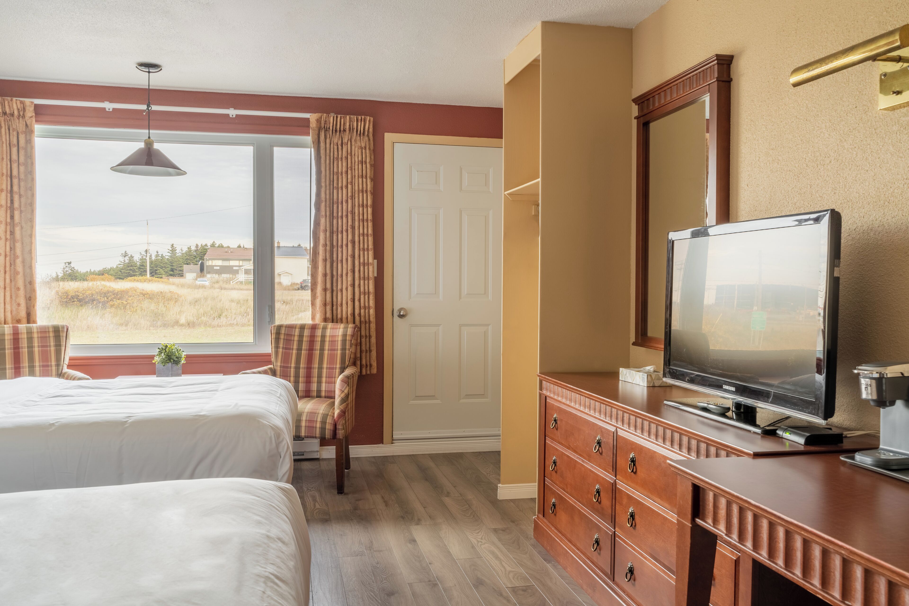 A hotel room with two beds, a television, a dresser, and a window with curtains.