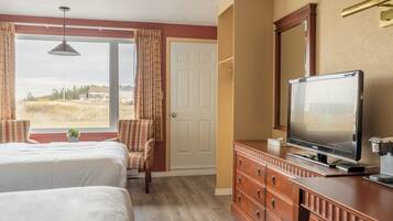 A hotel room with two beds, a television, a dresser, and a window with curtains.
