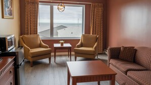 Ein Zimmer mit zwei Sesseln, einem Sofa, einem Holztisch und Meerblick durch ein großes Fenster.