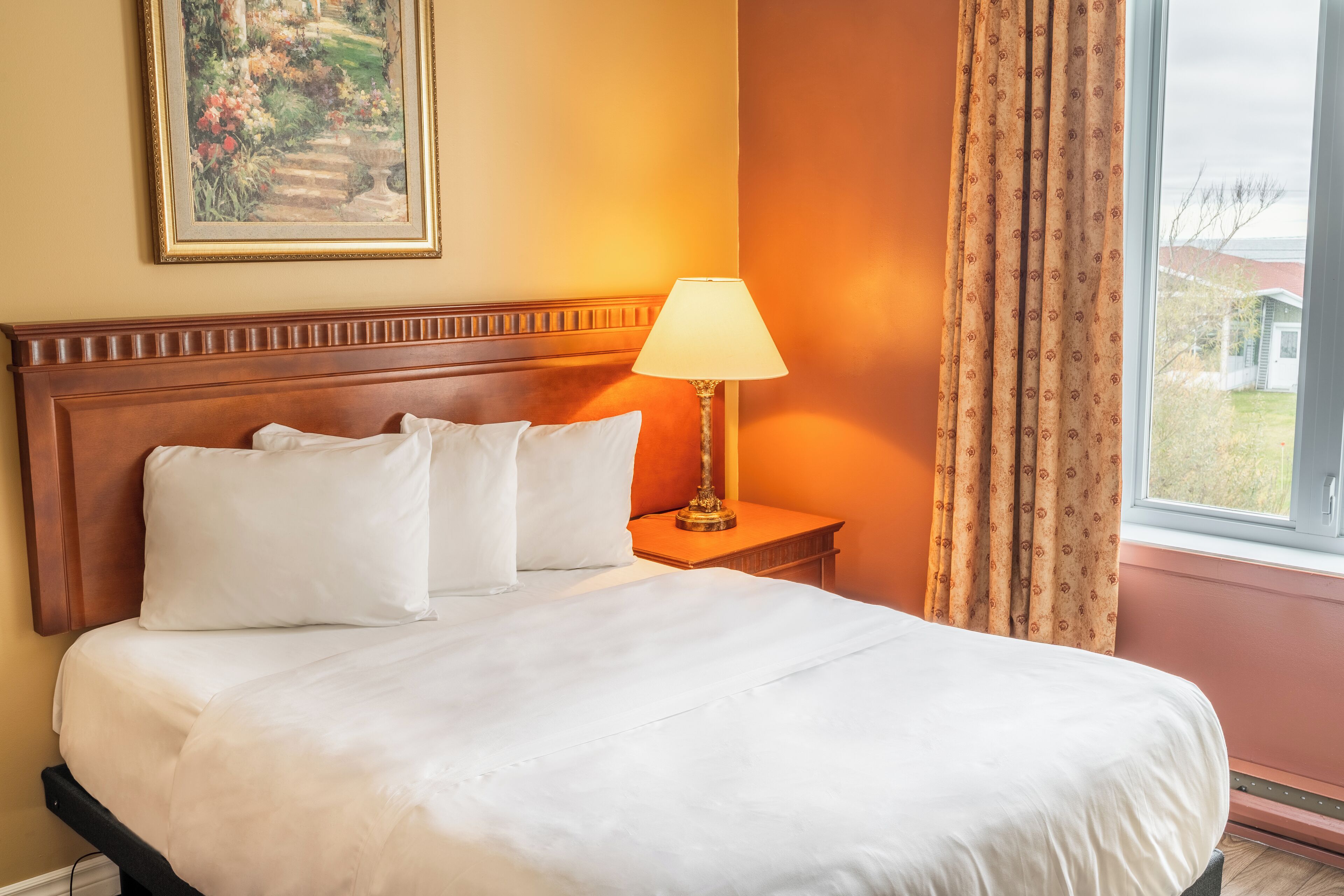 A neatly made bed with white linens, a wooden headboard, and a bedside table with a lamp.