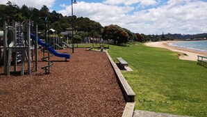 Ein Spielplatz mit Rutschen und Klettergerüsten, eine Rasenfläche und ein Strand im Hintergrund.